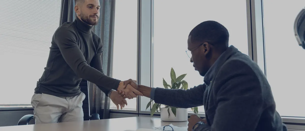 Two business people shaking hands at the start of a meeting by an office window
